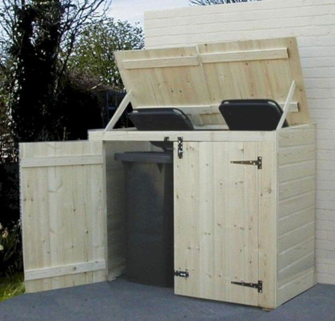 Light wood outdoor storage structure concealing two black trash bins with open lids.