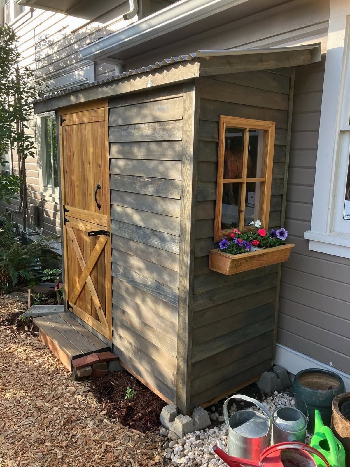 A small wooden lean-to shed with a window and flower box attached to a house.