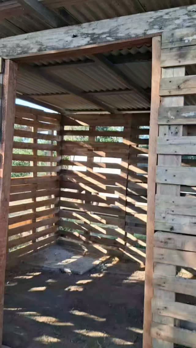 A small open structure constructed from reclaimed wooden pallet slats under a corrugated roof.