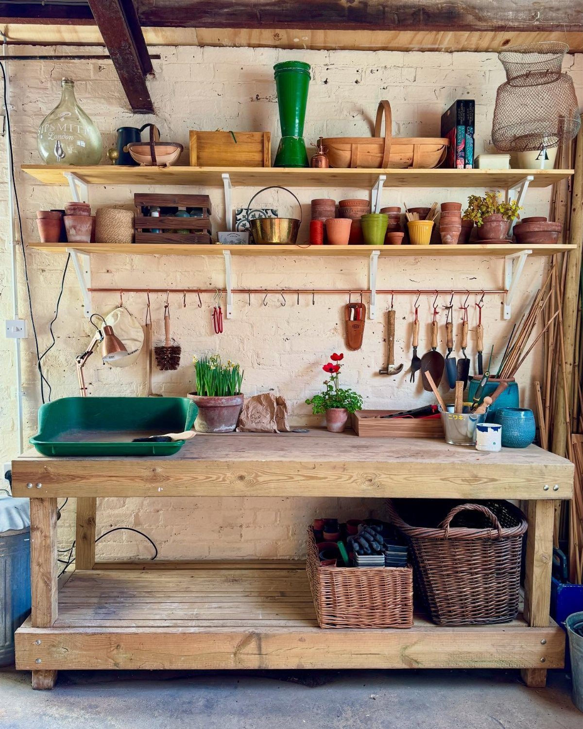 Wooden potting workbench with terracotta pots and gardening tools against a brick wall.