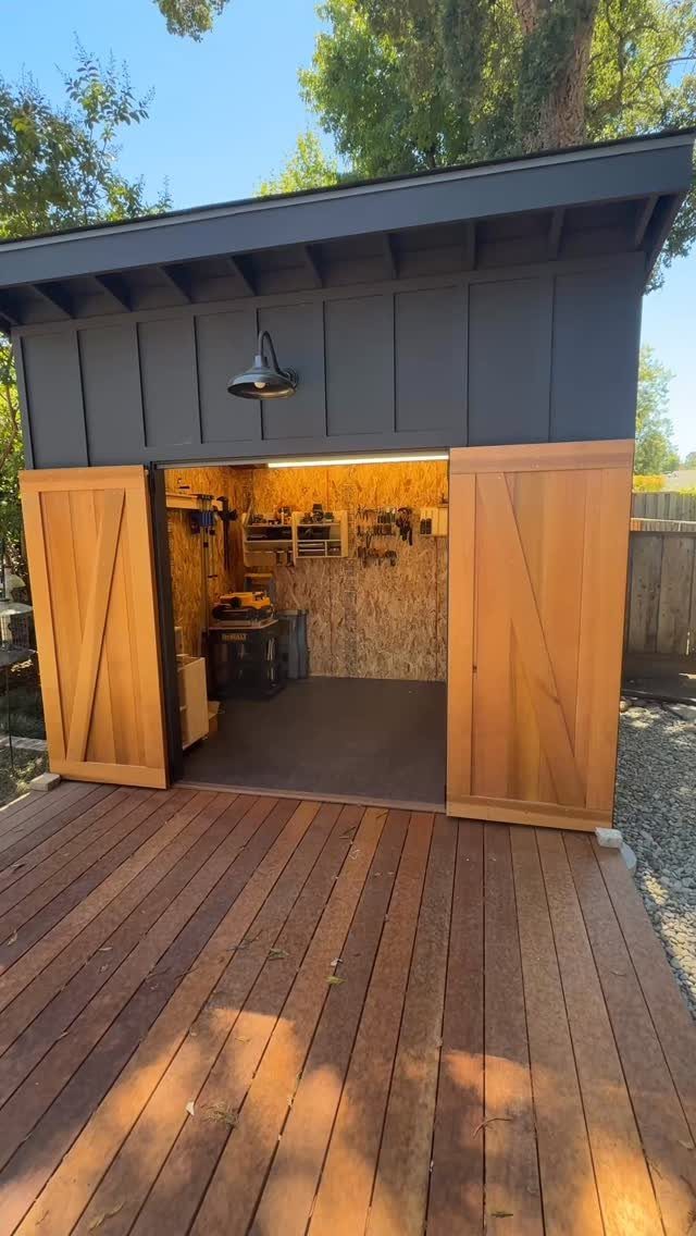 Open dark grey wooden shed with wooden doors revealing organized tools and shelves inside.
