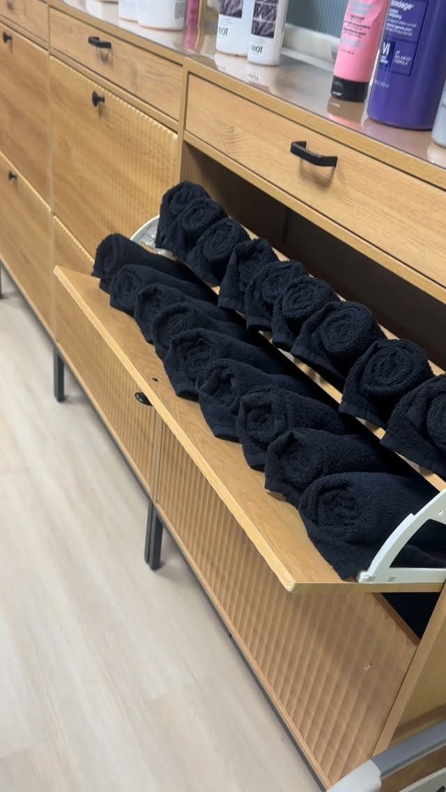 Rolled black towels organized neatly inside an open wooden drawer of a spa storage unit.