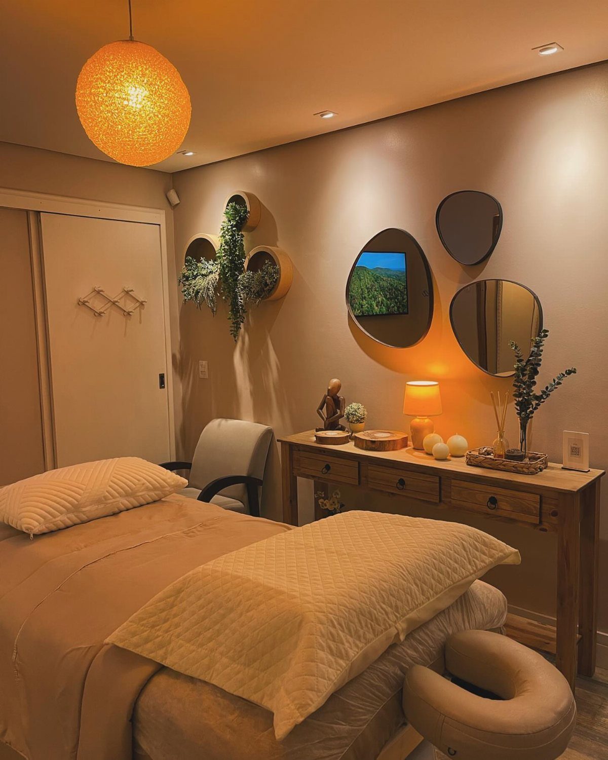A spa treatment room with a massage table, wooden console, and round wall mirrors.