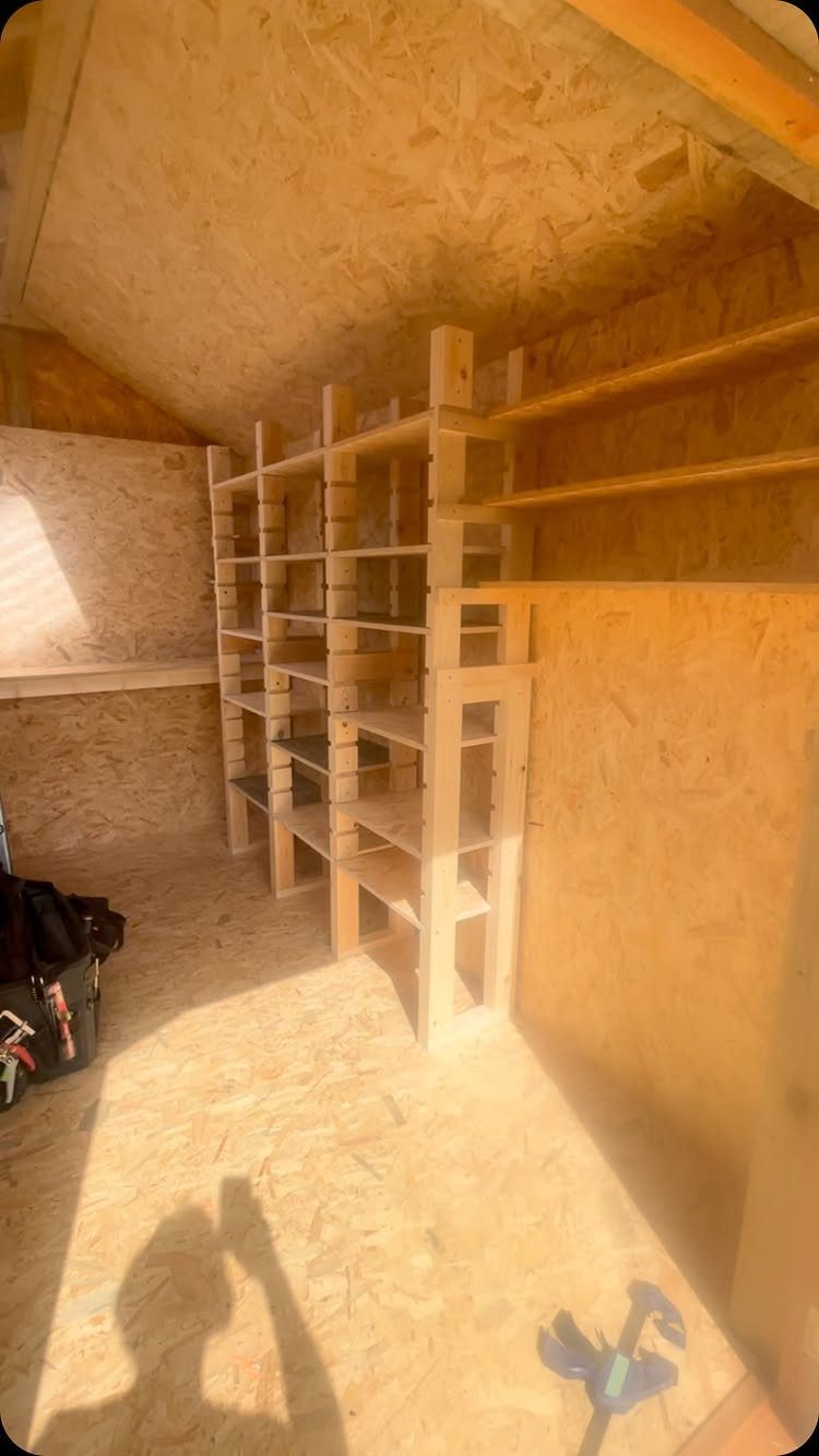 Wooden adjustable shelving units installed against the OSB walls inside an empty garden shed.