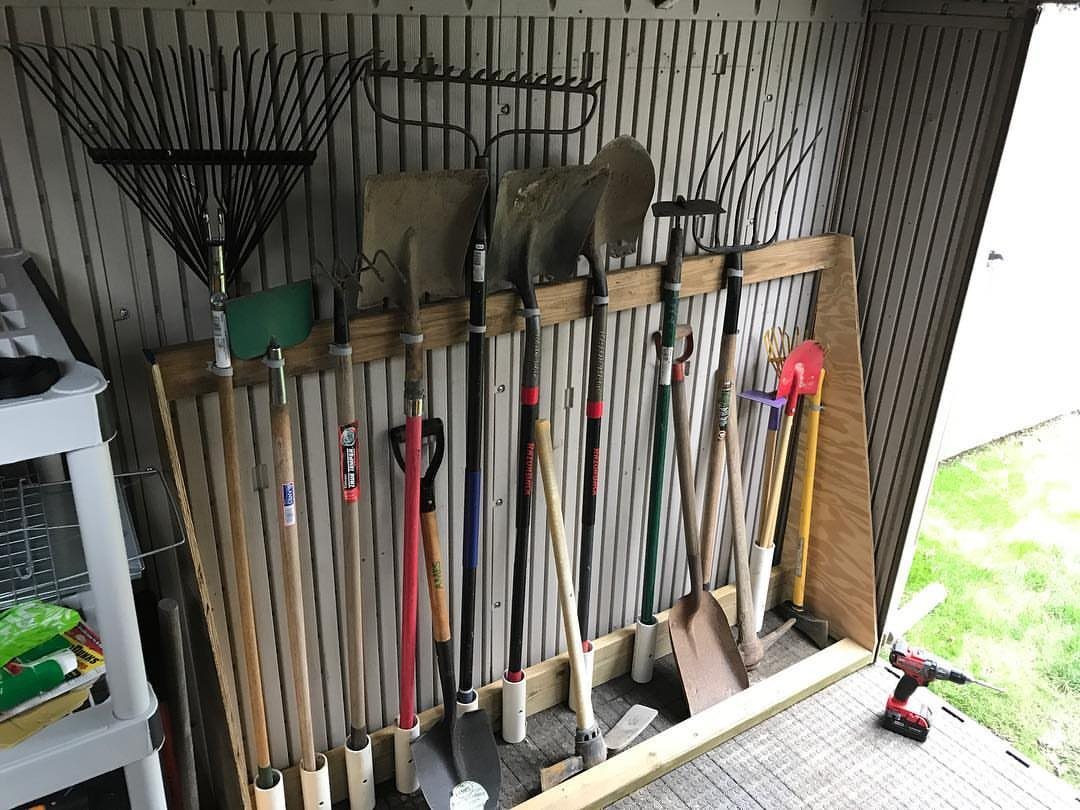 Garden tools like rakes and shovels organized in a wooden rack inside a shed.