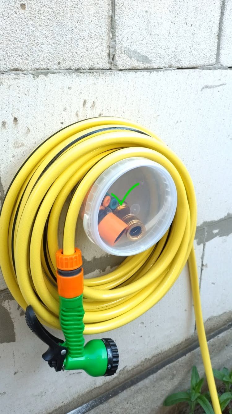 A coiled yellow garden hose with a green spray nozzle hanging on a brick wall.