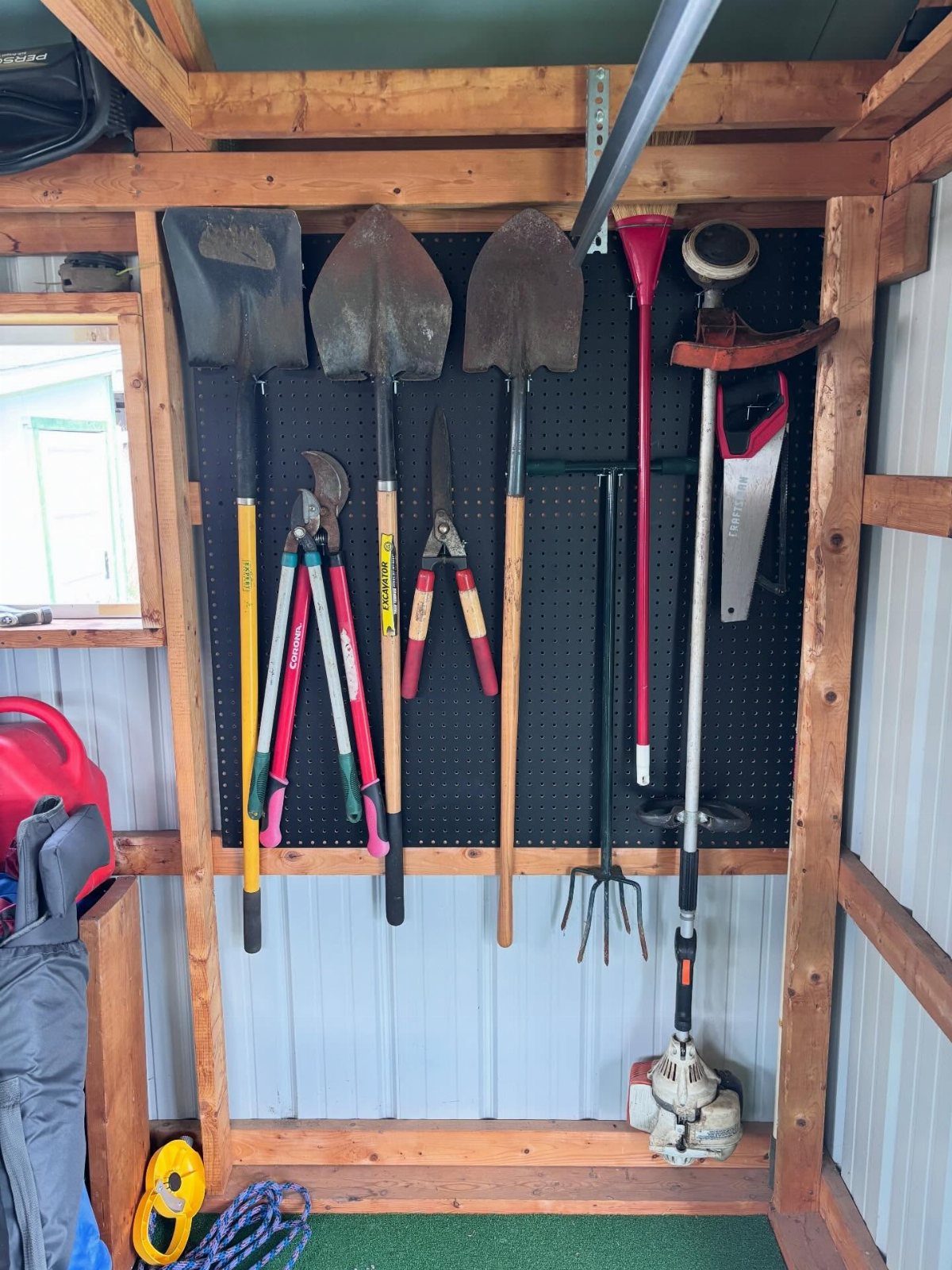 Garden tools hanging organized on a black pegboard inside a wooden garden shed.