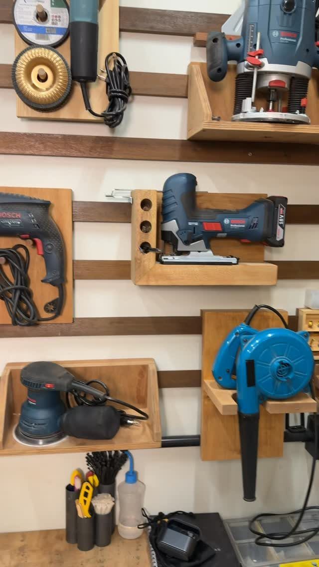 Power tools organized on custom wooden wall-mounted holders attached to a wooden slatwall system.