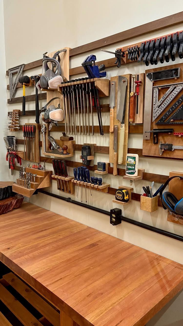 Hand tools organized on a wooden slatwall system above a large wooden workbench.