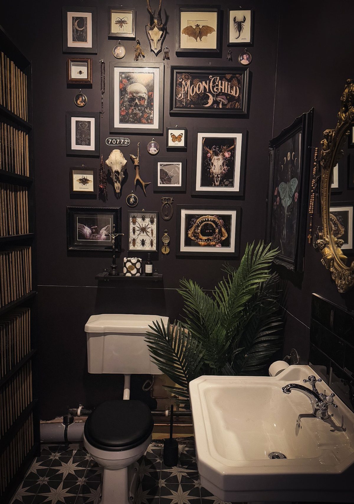 A dark bathroom wall decorated with a diverse gallery wall of framed art and small objects.