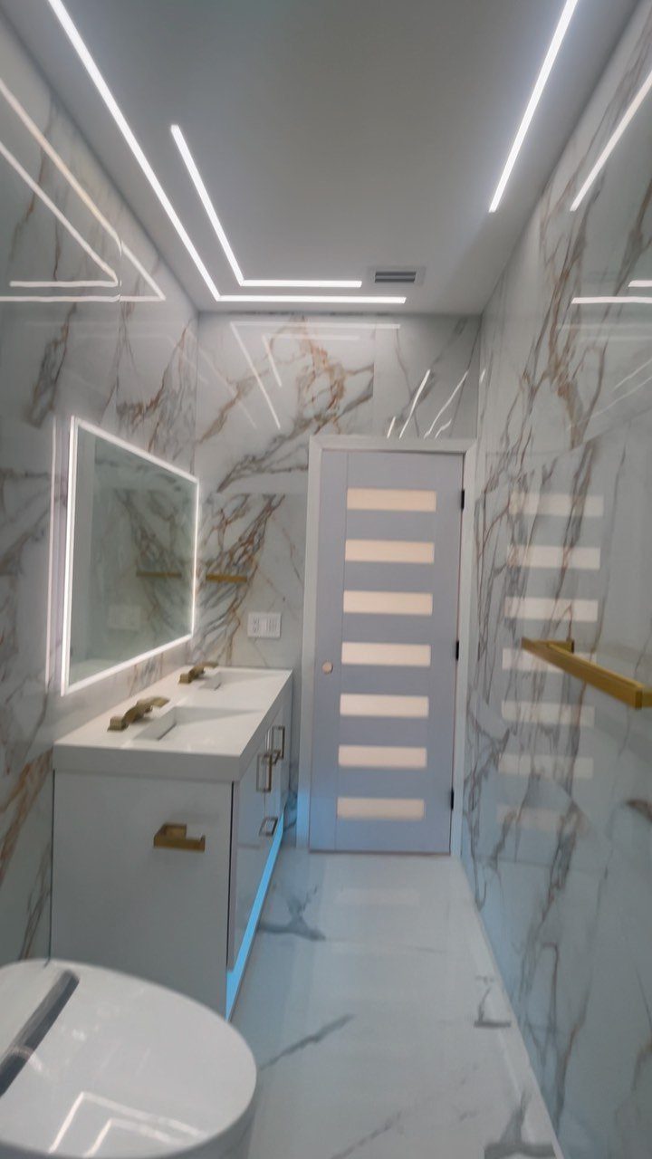 A modern bathroom featuring marble walls, a white vanity, and a glowing LED rectangular mirror.