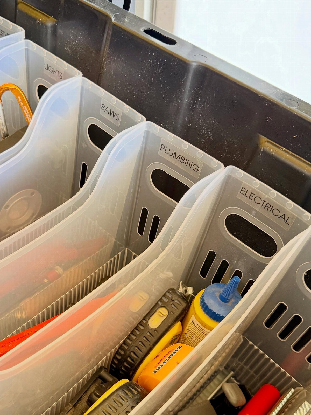Clear plastic bins labeled with categories containing various hand tools inside a black storage container.