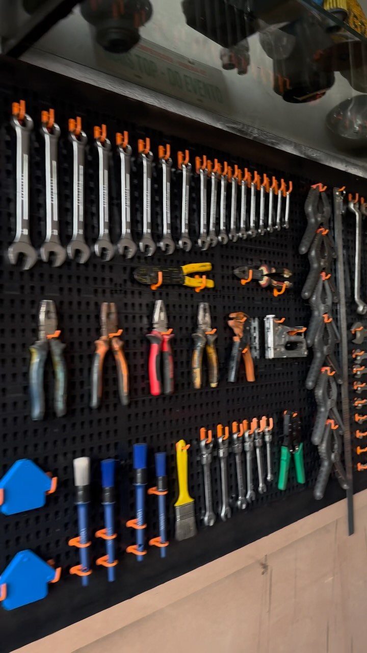 Various hand tools organized on a black pegboard using orange hooks and holders.
