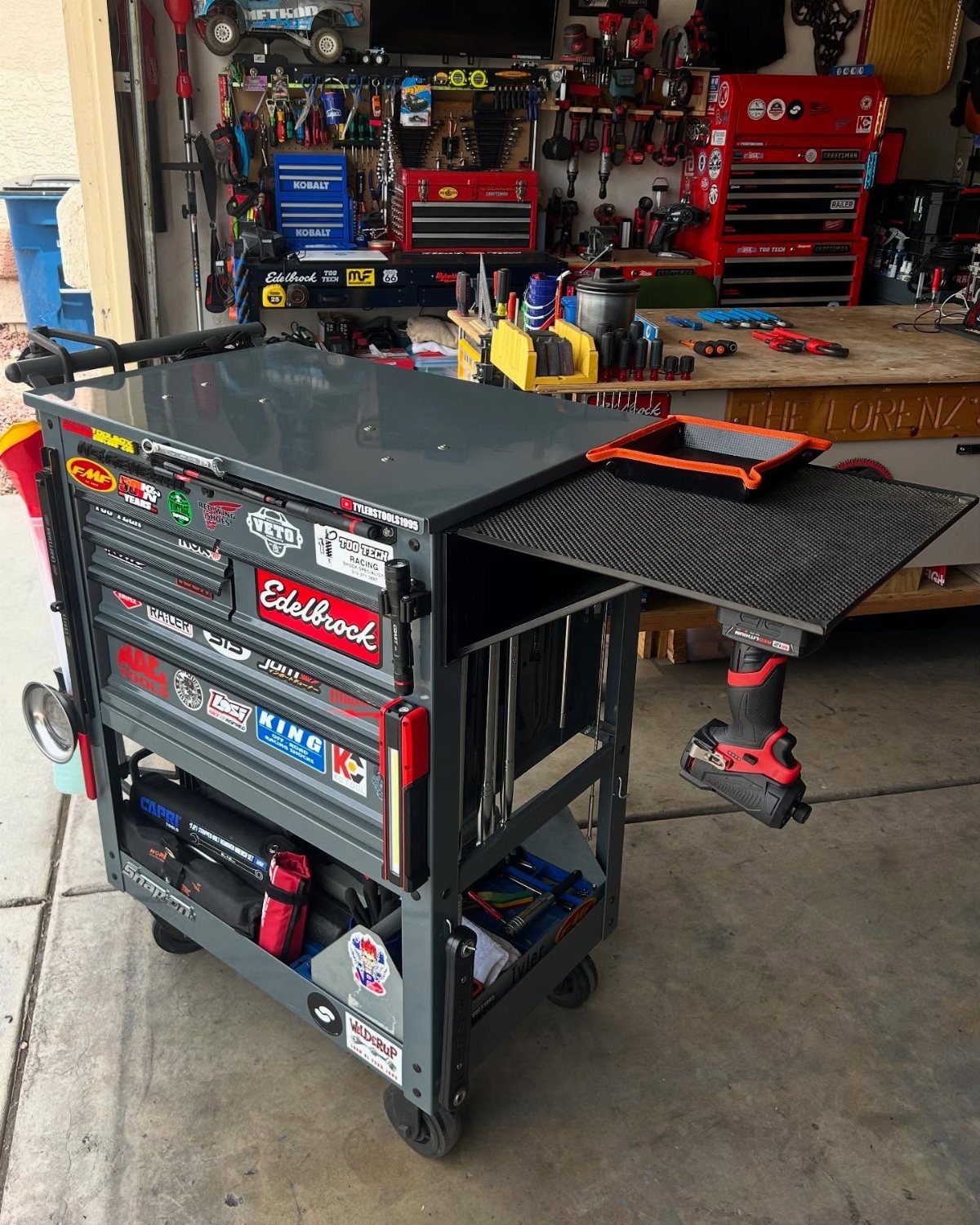 A grey metal rolling tool cart with stickers and an extended side work surface in a garage.