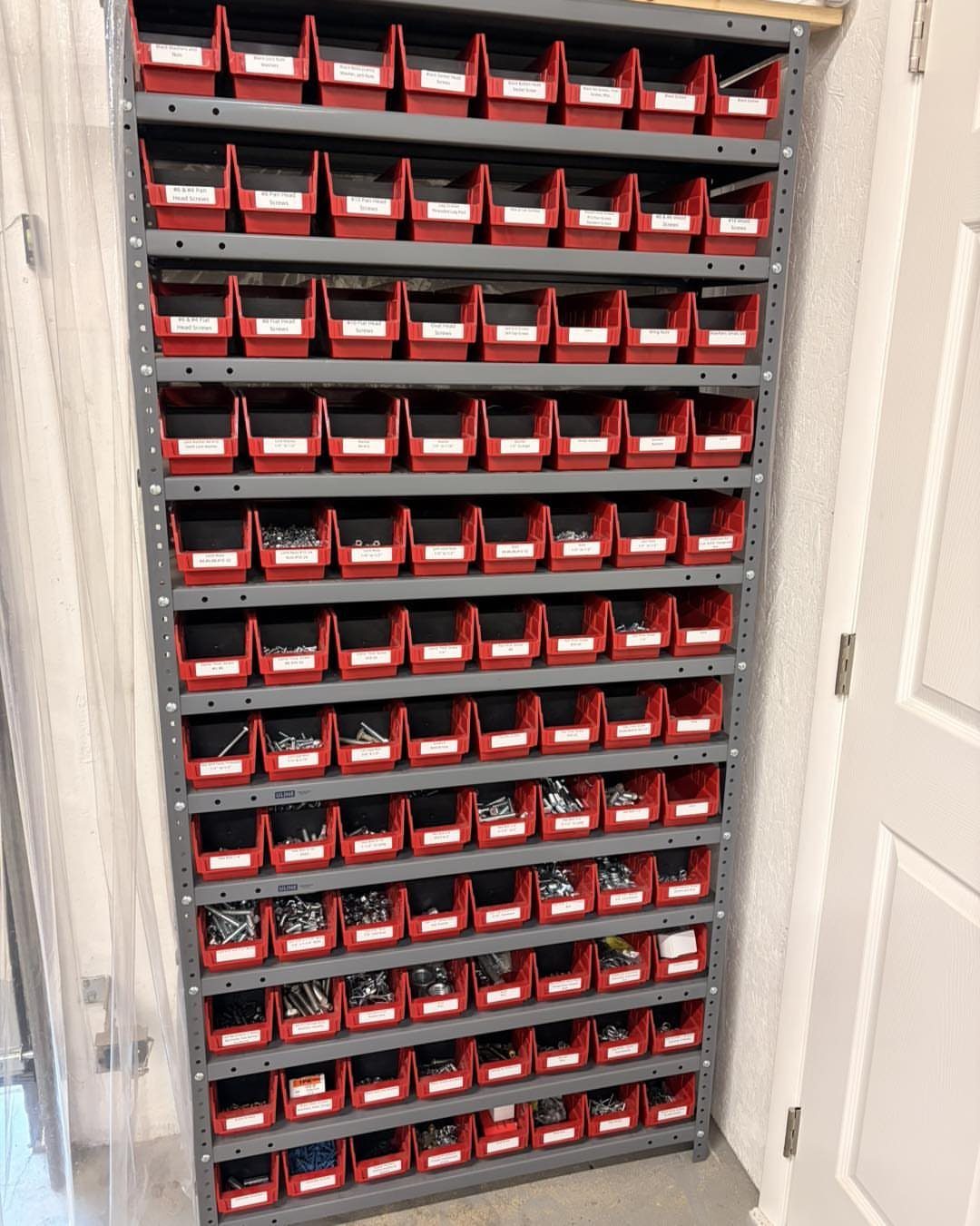Red plastic hardware bins organized on a tall grey metal shelving unit in a workshop.
