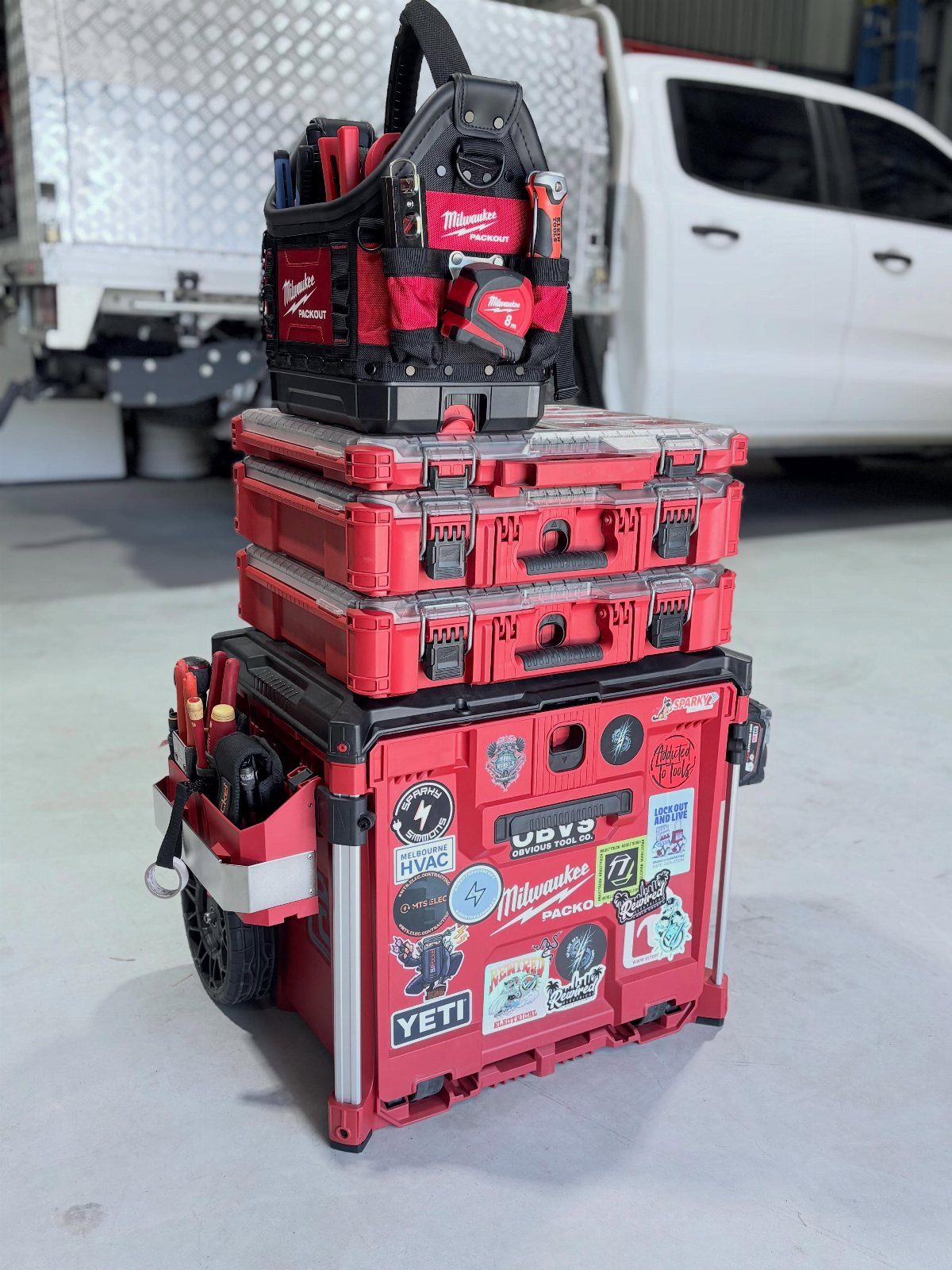 Stacked red and black modular tool storage boxes sitting on a concrete floor near a white truck.