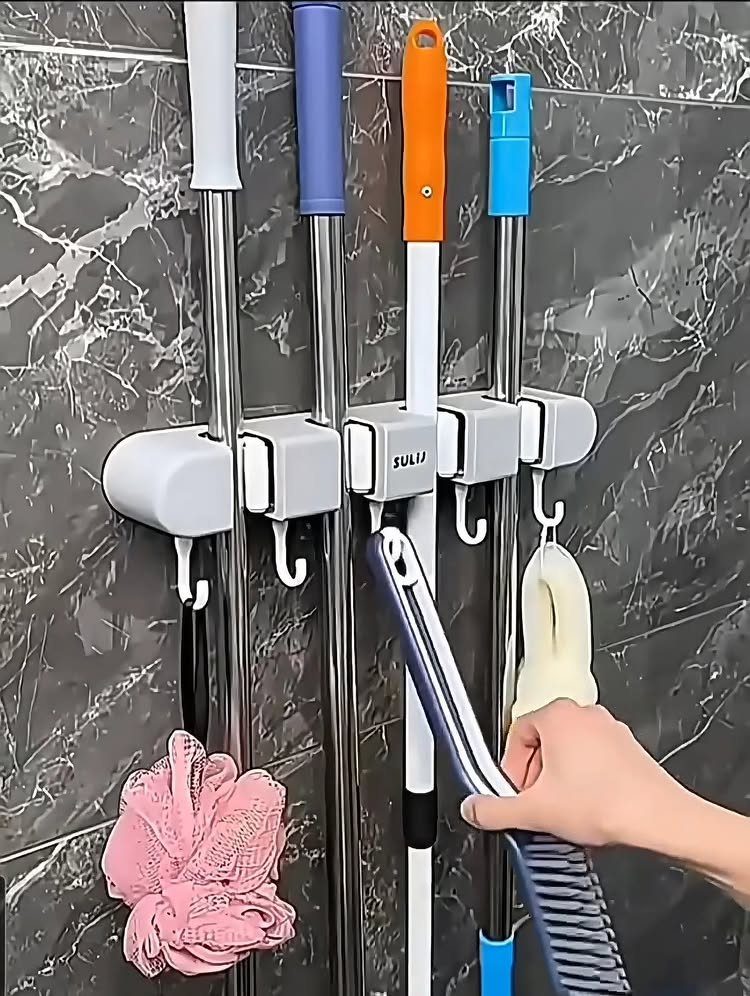 White wall-mounted holders securing various brooms and mops against a dark marble wall.