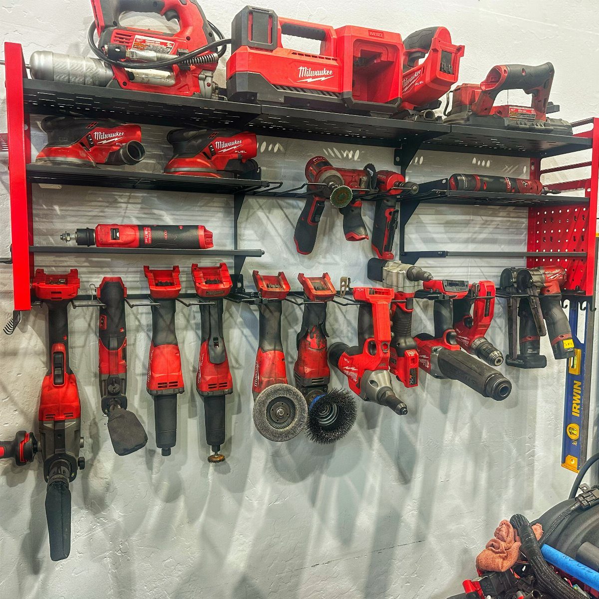 Red power tools hanging on black metal racks and organized on shelves against a white wall.