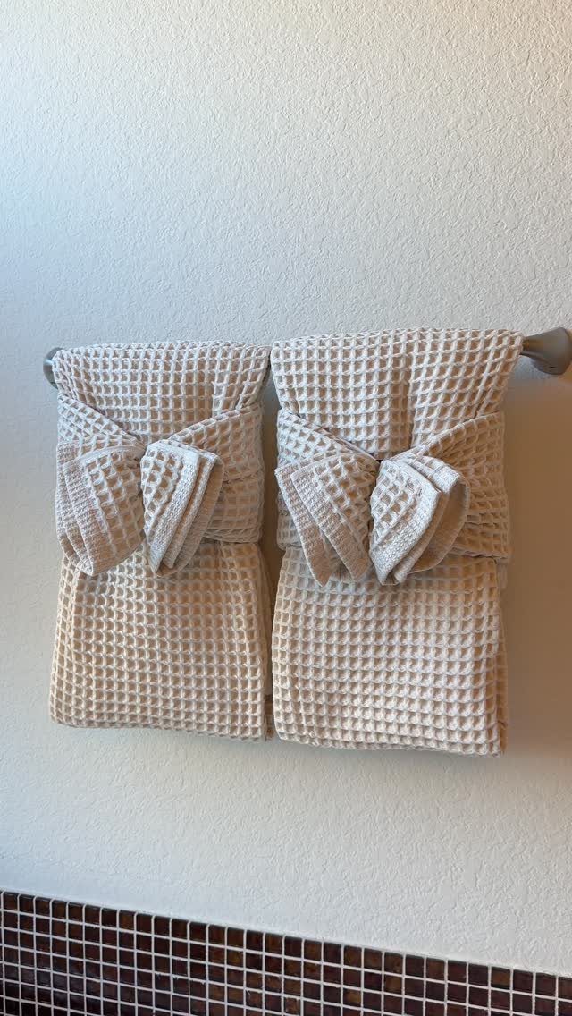 Two beige waffle-weave towels folded into bows hanging on a silver towel bar.