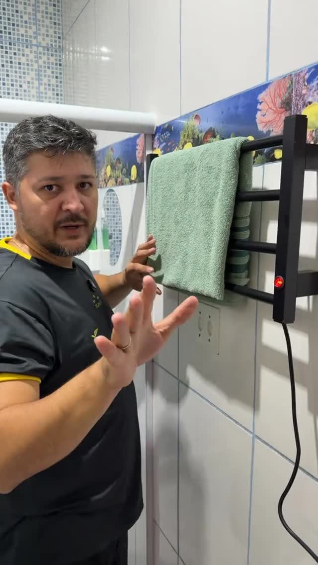 A man gestures toward a black heated towel rack with a green towel in a bathroom.