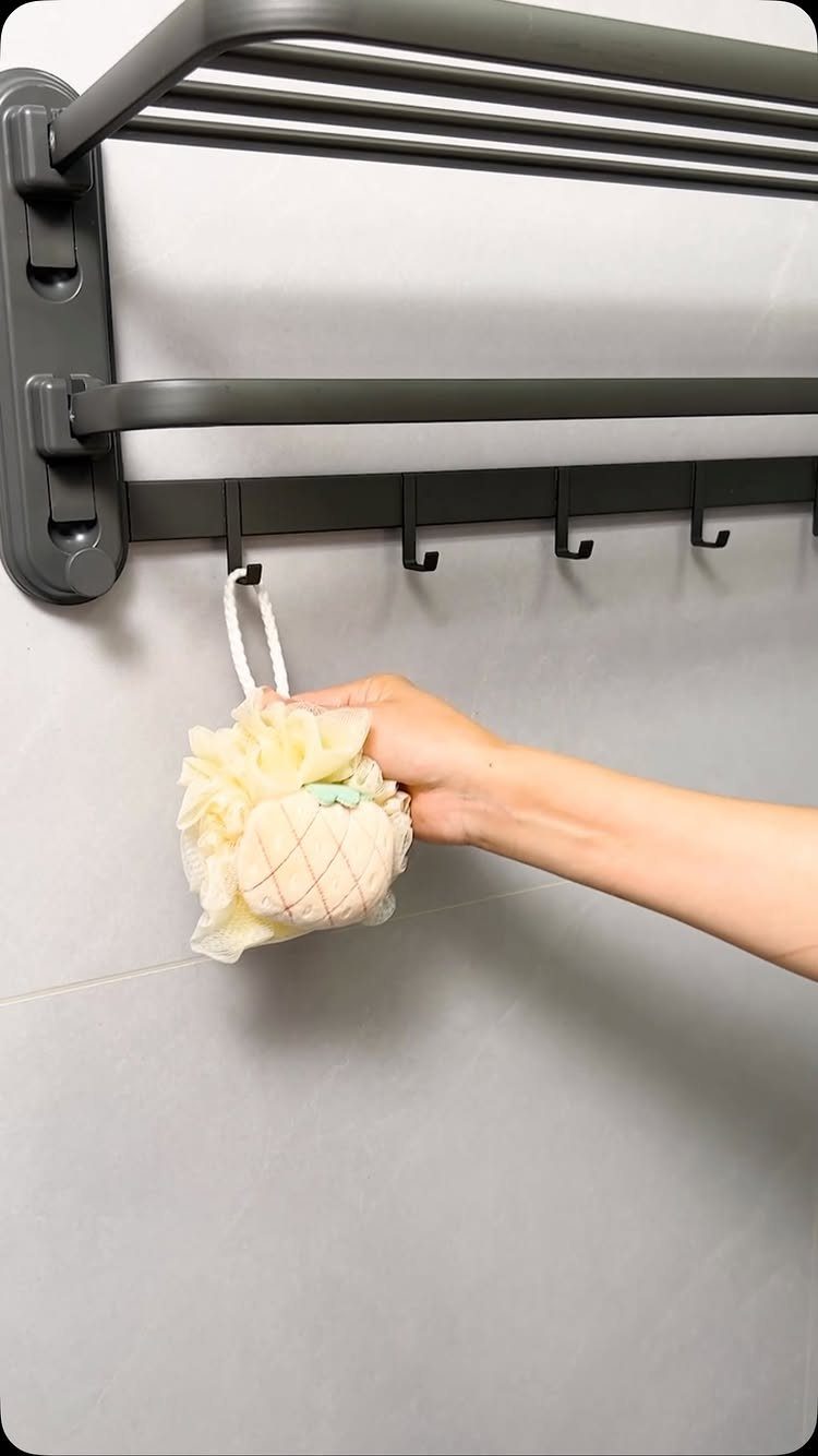 A hand hanging a white bath sponge onto a grey multi-tier metal towel rack.