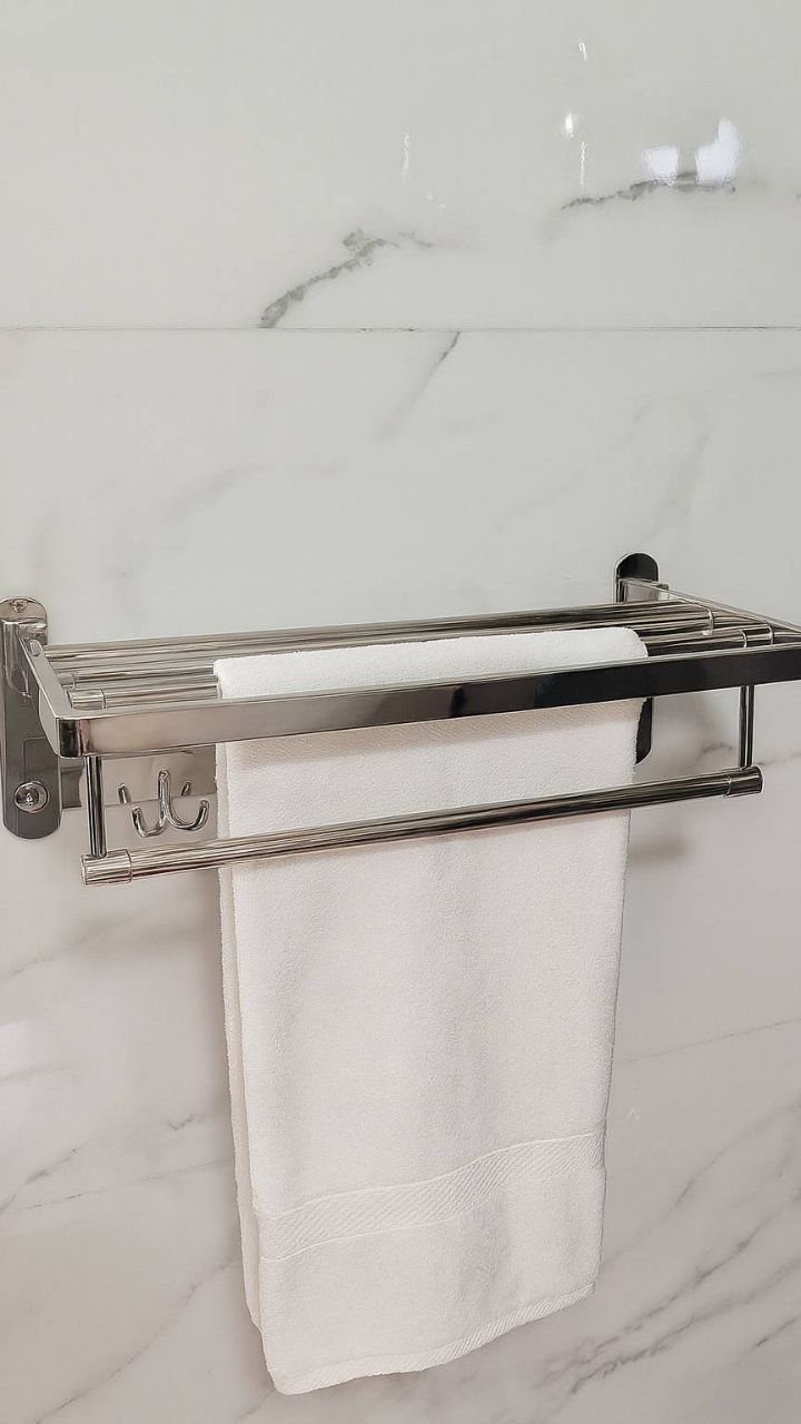 Chrome metal shelf with an integrated towel bar hanging a white towel on marble.