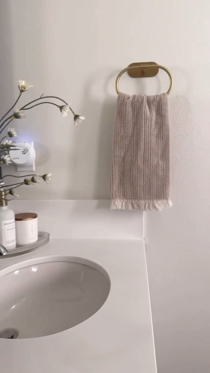 A gold circular towel ring holding a beige fringed towel on a white bathroom wall.
