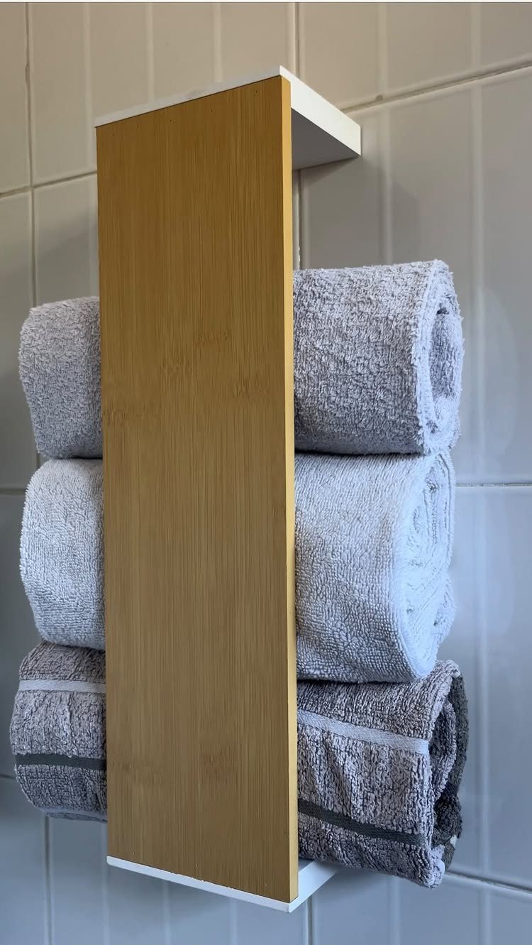 Three grey rolled towels hanging on a vertical wooden towel rack against a white tiled wall.