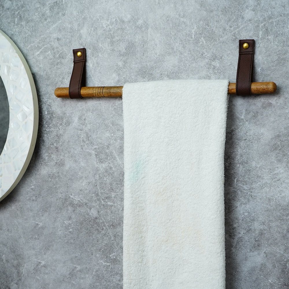 A wooden towel bar with leather straps holding a white towel against a grey wall.