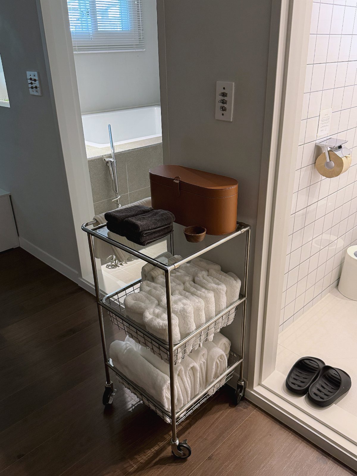 A silver metal rolling trolley filled with neatly folded white and dark towels in a bathroom.
