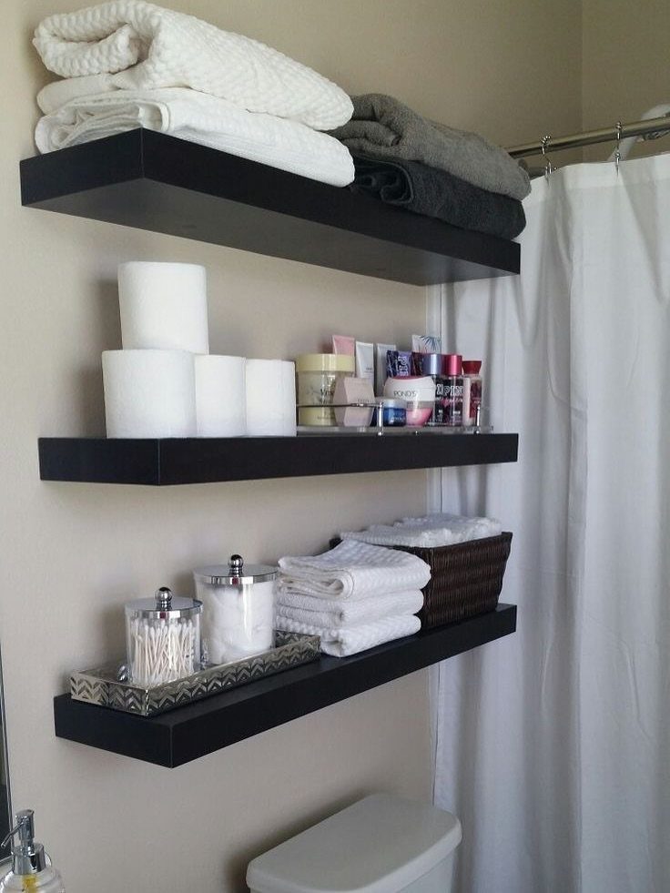 Three black floating shelves mounted on a wall holding towels and bathroom supplies.