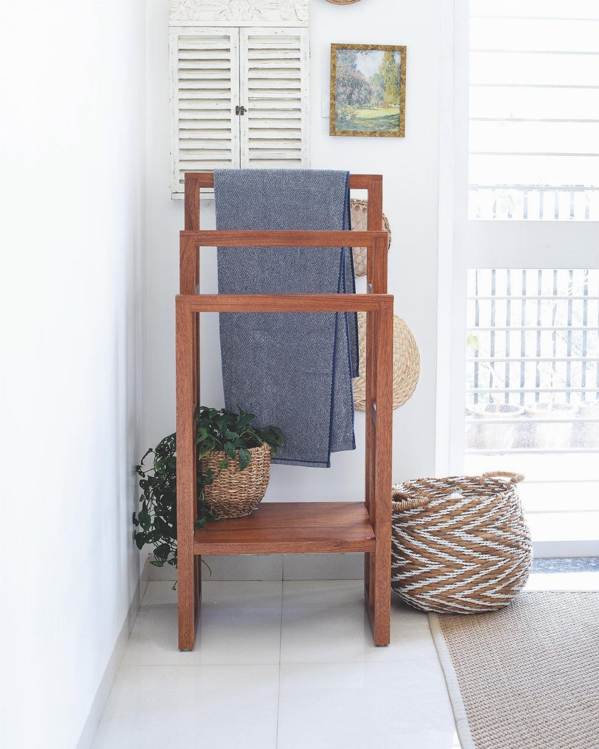 A wooden freestanding towel rack with a blue towel and a small potted plant.