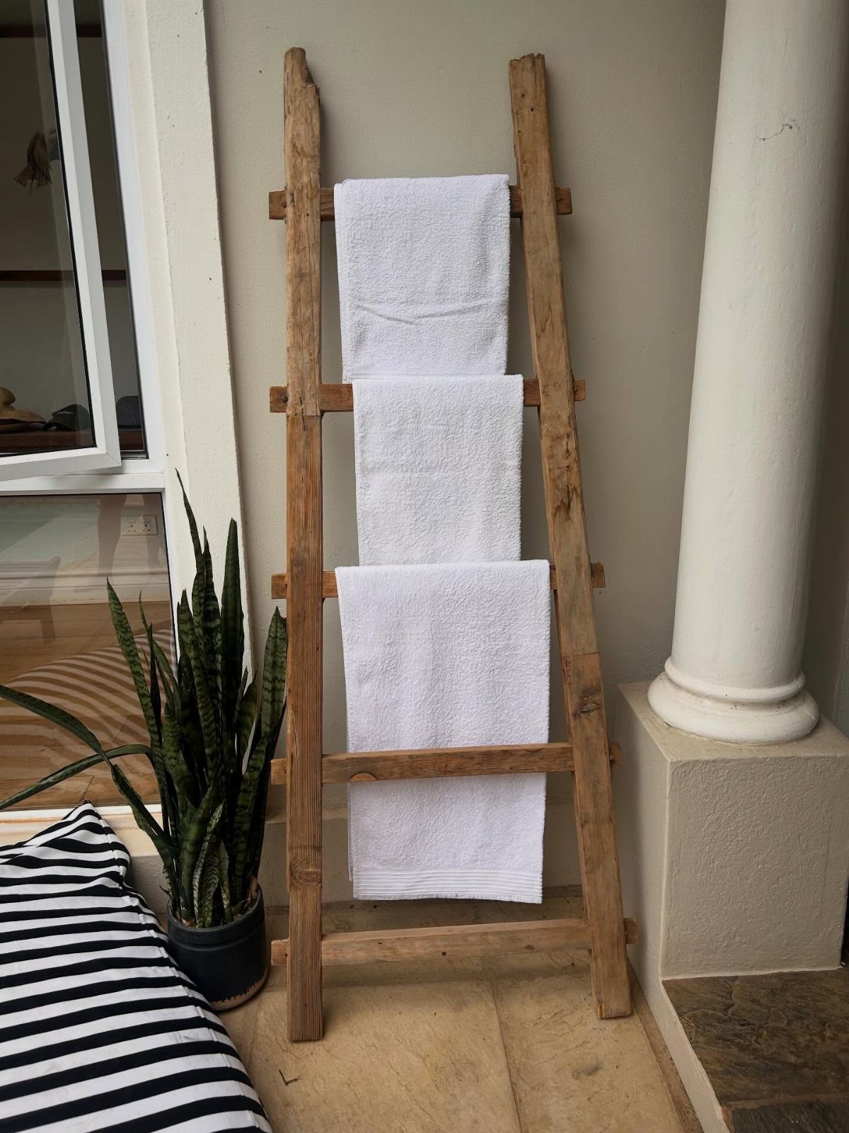 A wooden ladder leaning against a wall with white towels hanging on the rungs.