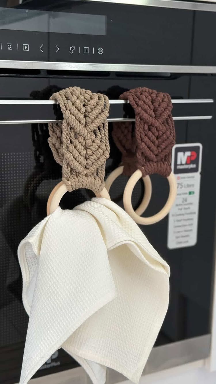 Macrame towel holders with wooden rings hanging from a black bar holding a white towel.