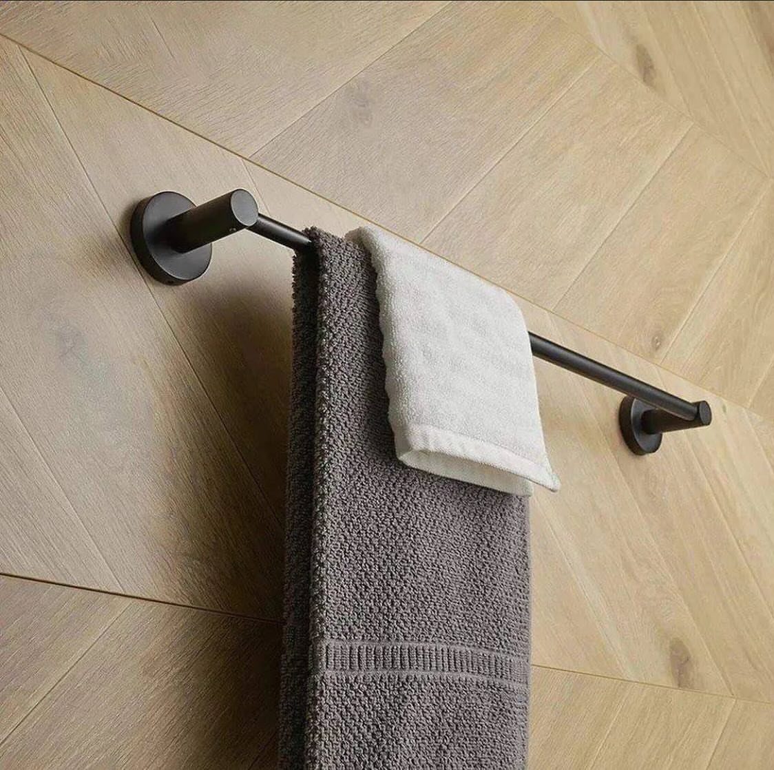 A dark metal towel bar holding grey and white towels on a wooden wall.