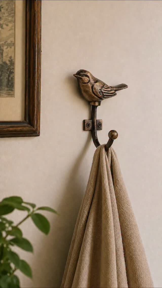A bird-shaped bronze metal towel hook mounted on a wall with a beige towel hanging from it.