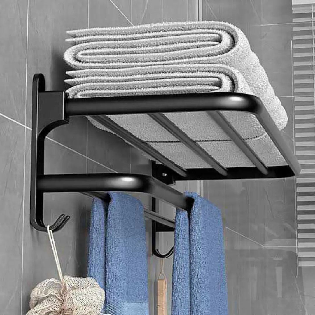 Black metal towel rack with folded grey towels and hanging blue towels on grey tiles.