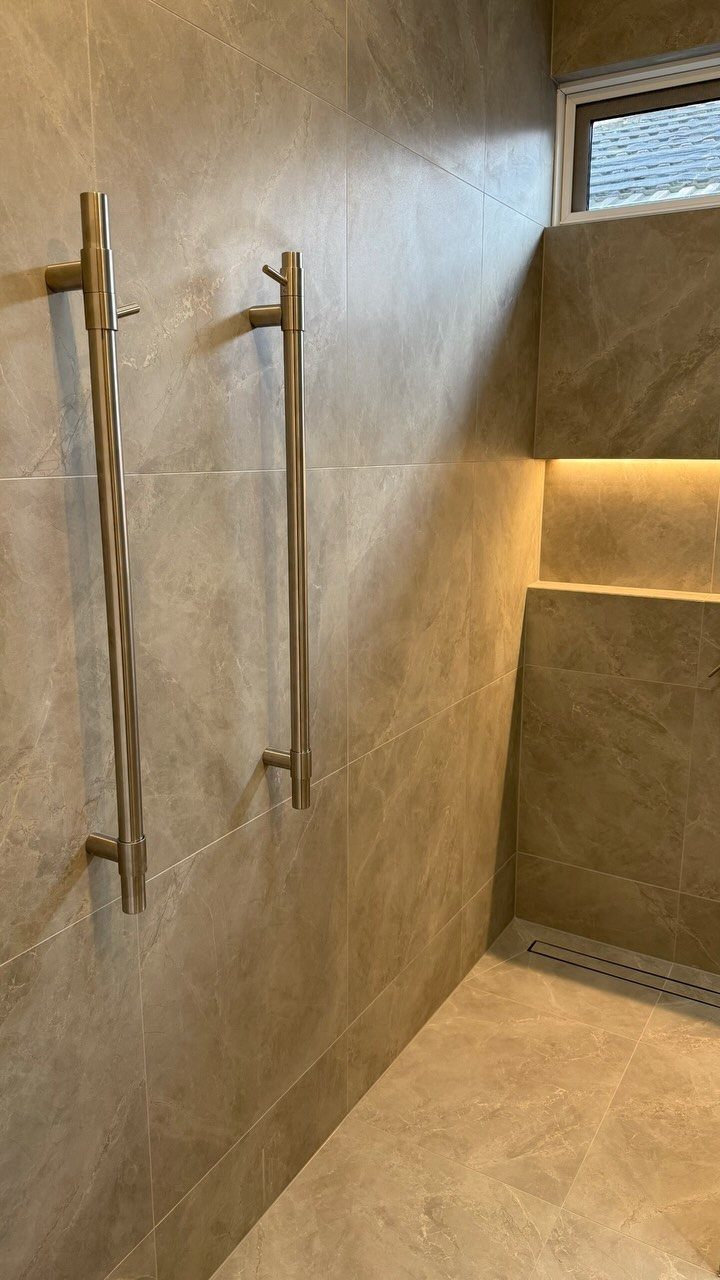 Two vertical bronze towel bars mounted on a beige tiled bathroom wall.
