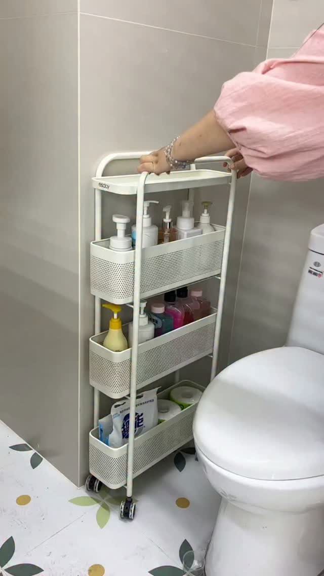 A white three-tier rolling cart filled with toiletries stands next to a white toilet.