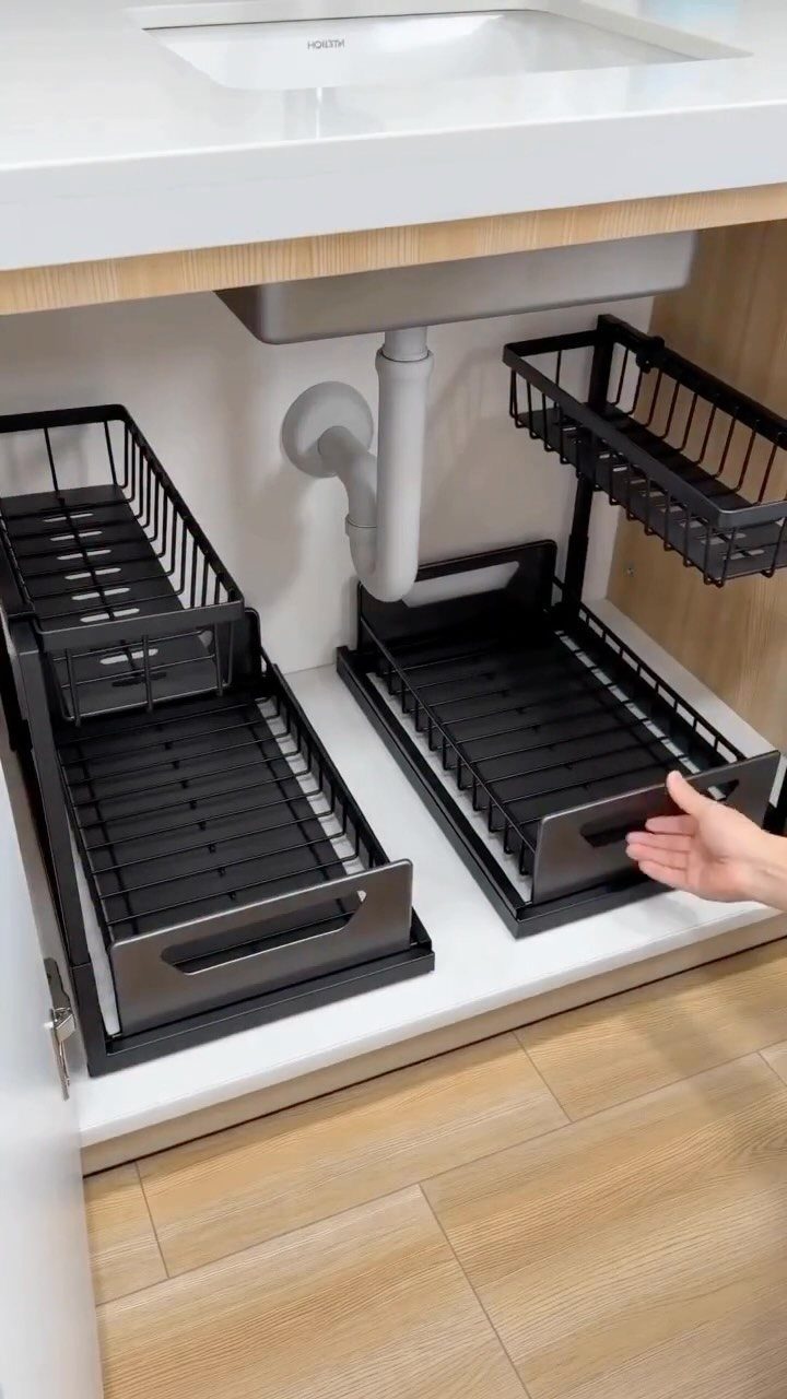 Black tiered sliding shelf units being pulled out from under a white bathroom sink cabinet.