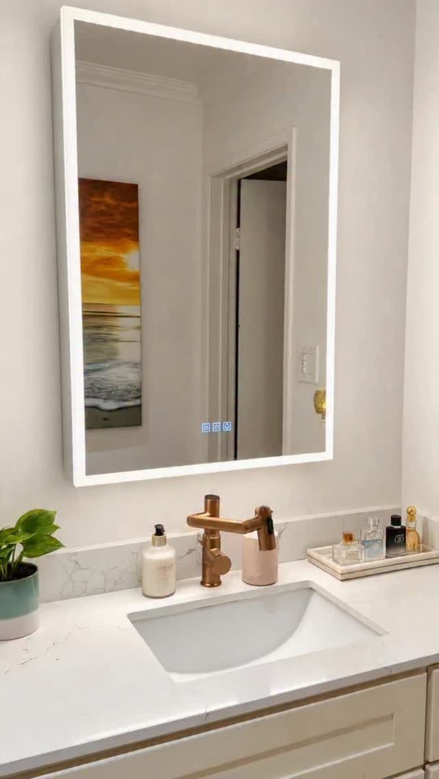 A rectangular LED-lit mirror hangs above a white marble bathroom vanity with a gold faucet.