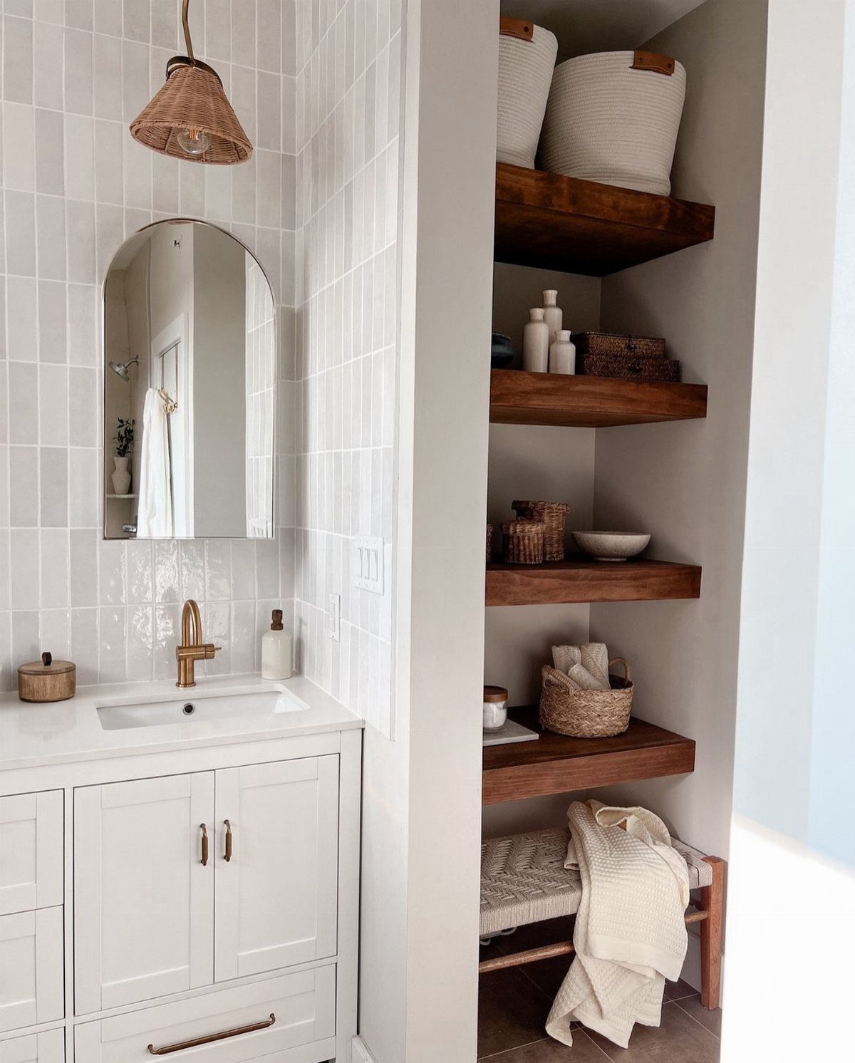 White bathroom vanity with an arched mirror next to recessed wooden open shelving units.