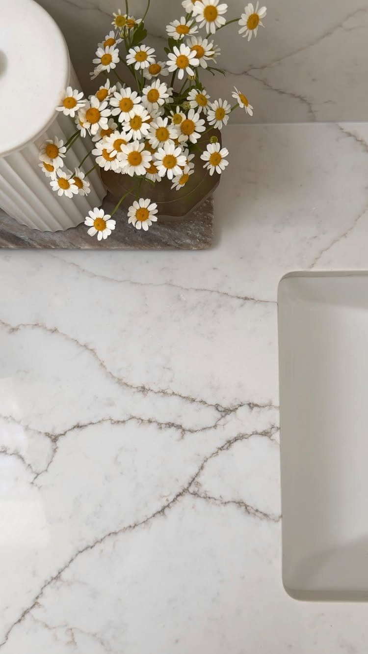 White quartz countertop with dramatic grey veining, a white sink, and daisies in a vase.