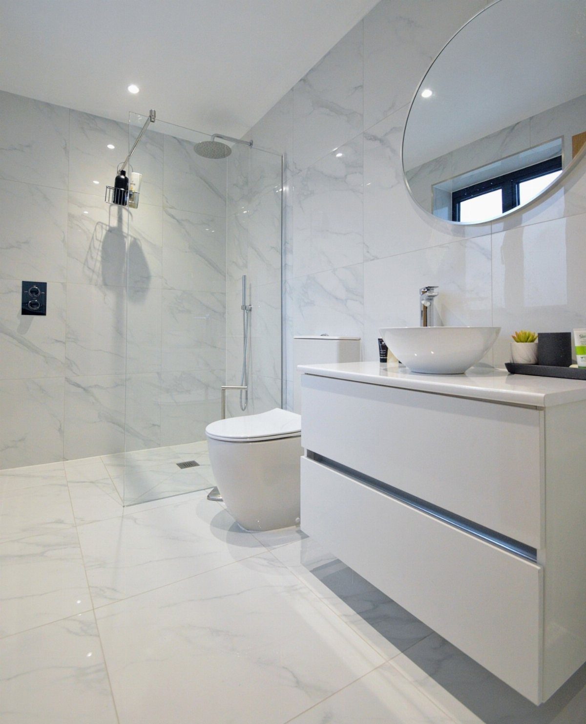 White marble tiles covering the walls and floor of a modern, bright bathroom.