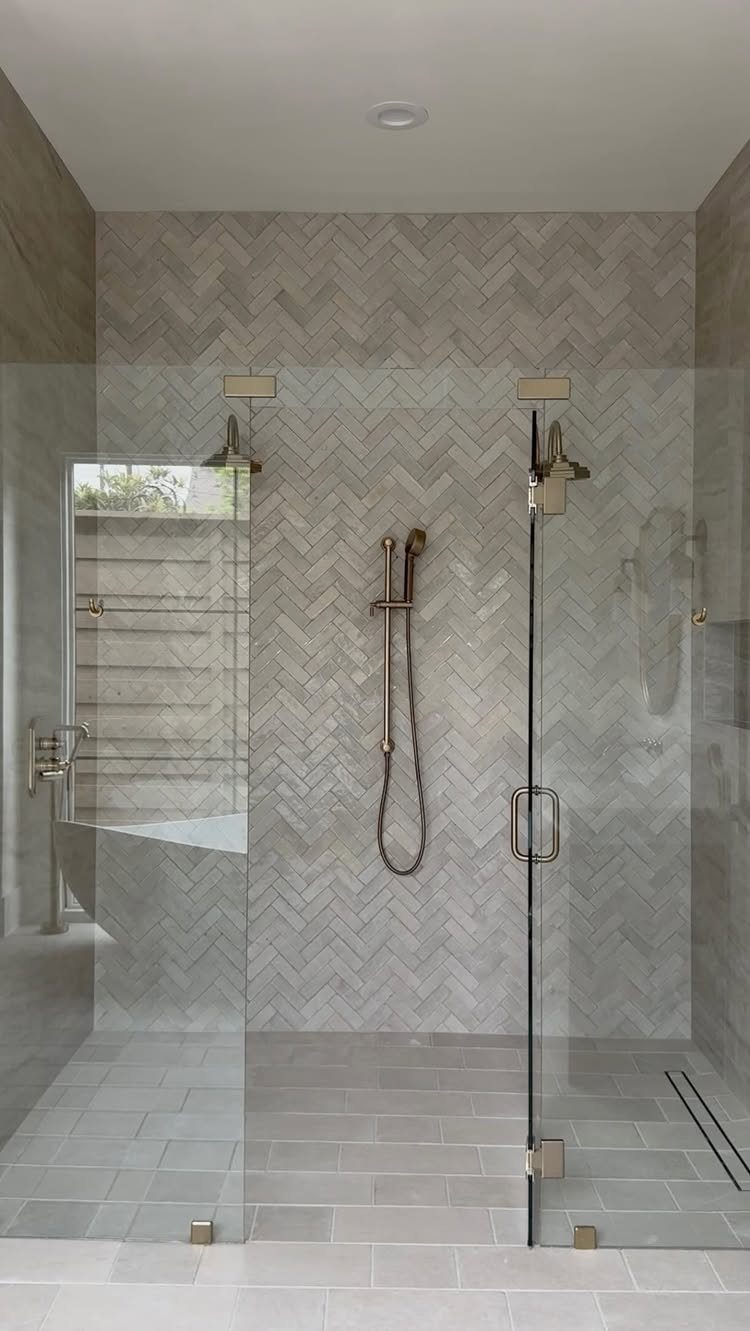 Light grey herringbone tiles covering the walls of a modern glass walk-in shower.